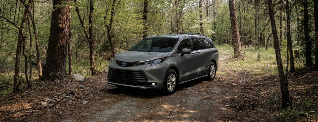 The front and side view of a Cement Gray 2022 Toyota Sienna Woodland Special Edition parked under a set of trees on a trail.