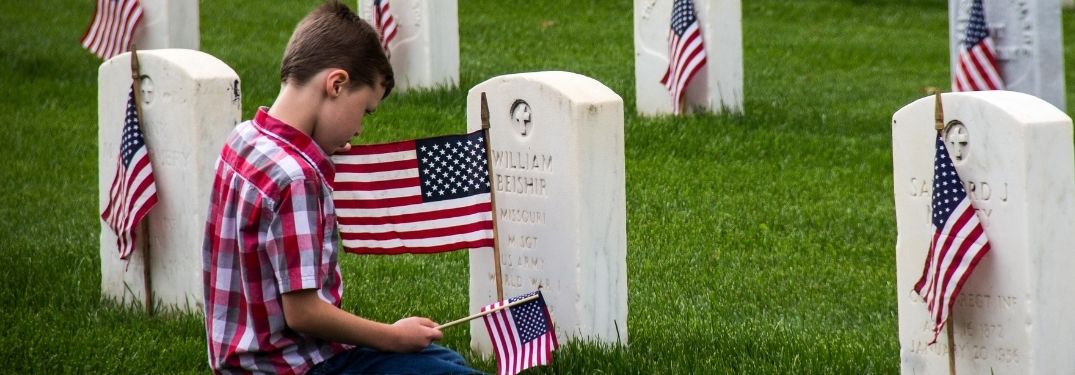 Boy Kneeling by a Headstone with American Flags on Memorial Day
