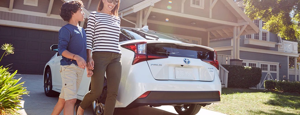 A mom and her son standing in front of white Prius in the driveway of a nice home.