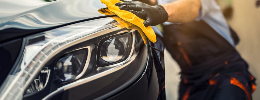 A man waxing a black crossover SUV with a yellow cloth.