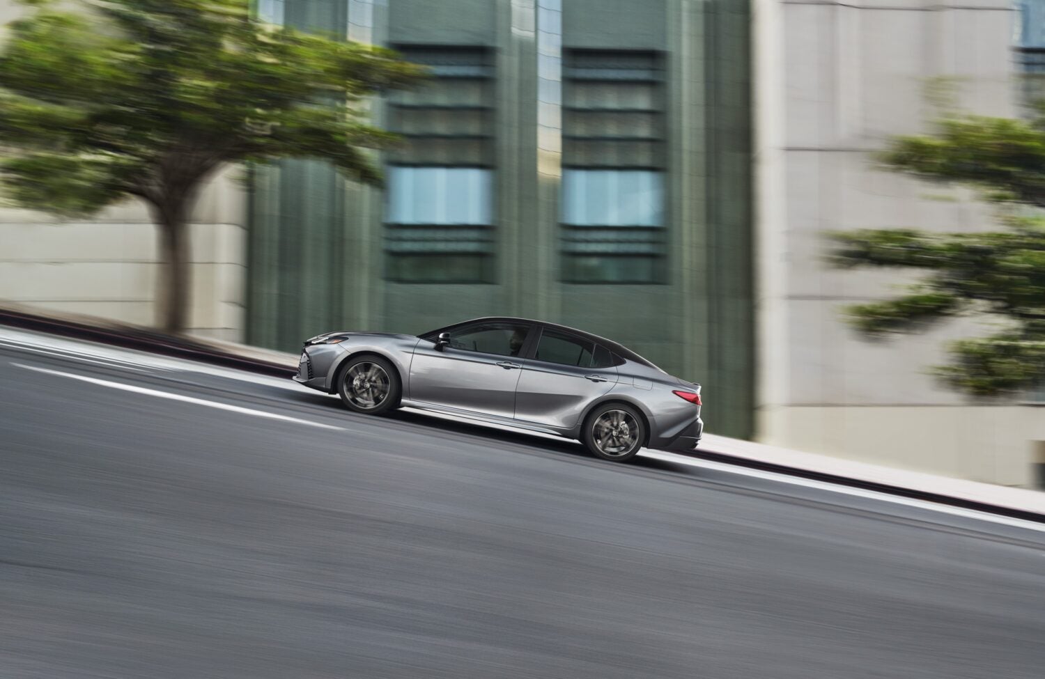 The silver 2026 Camry in Phoenix drives up a hill to the left on a sloped city street.