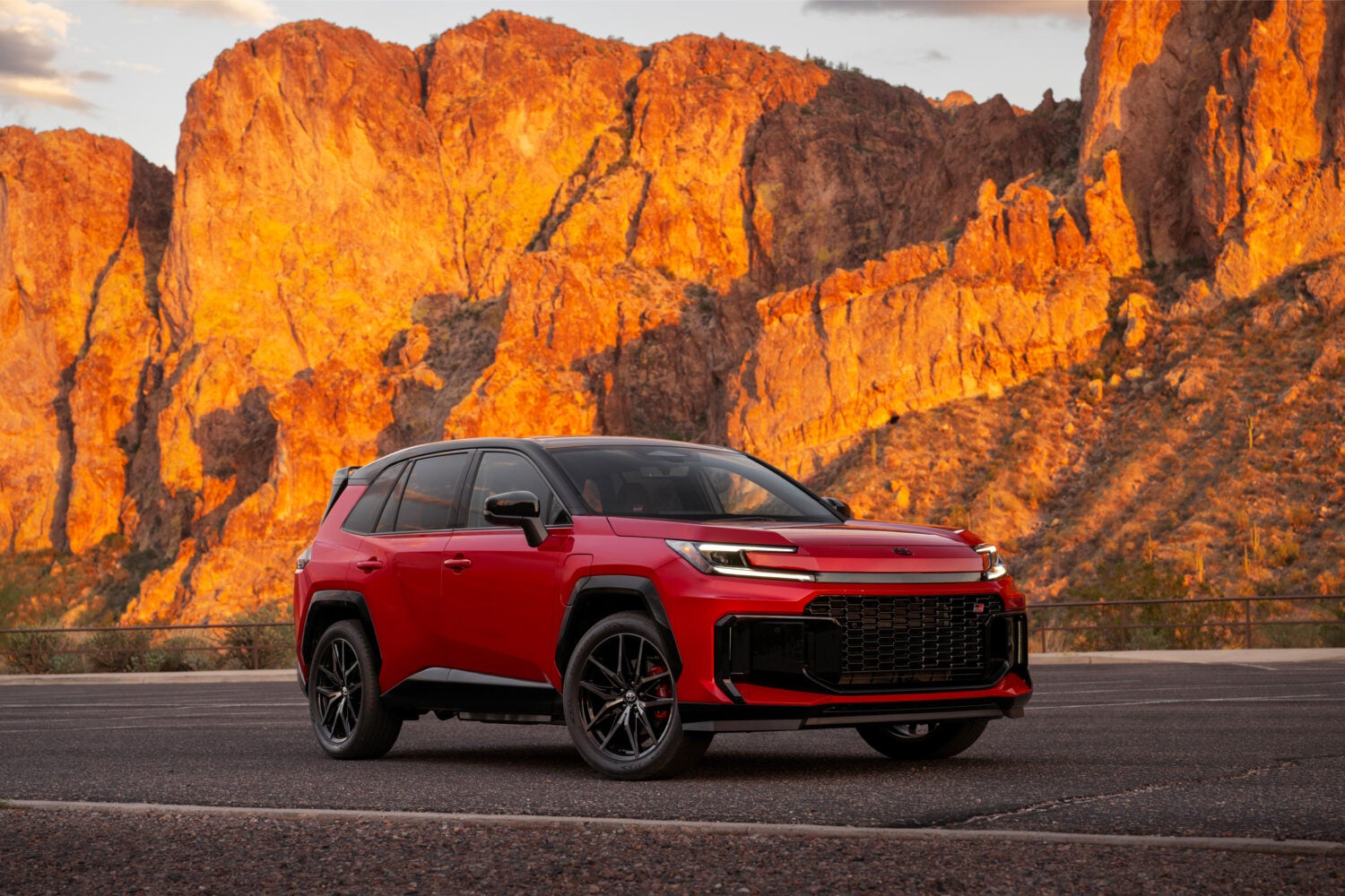A red 2026 Toyota Rav4 GR Sport in Phoenix is parked facing the viewer to the right on a desert road with an orange mountain lit up by the sunset in the background.