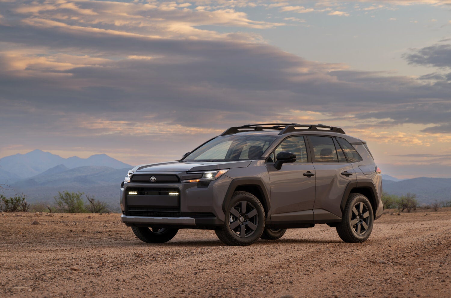 A grey new Toyota Rav4 Woodland in Phoenix is parked facing the viewer to the left on a desert dirt road at sunset.